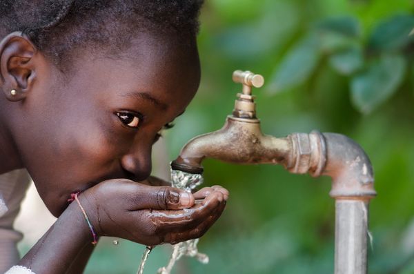 A child drinking water from a faucet